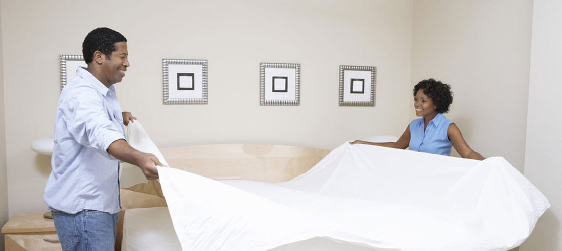 Couple making a bed with white bedding