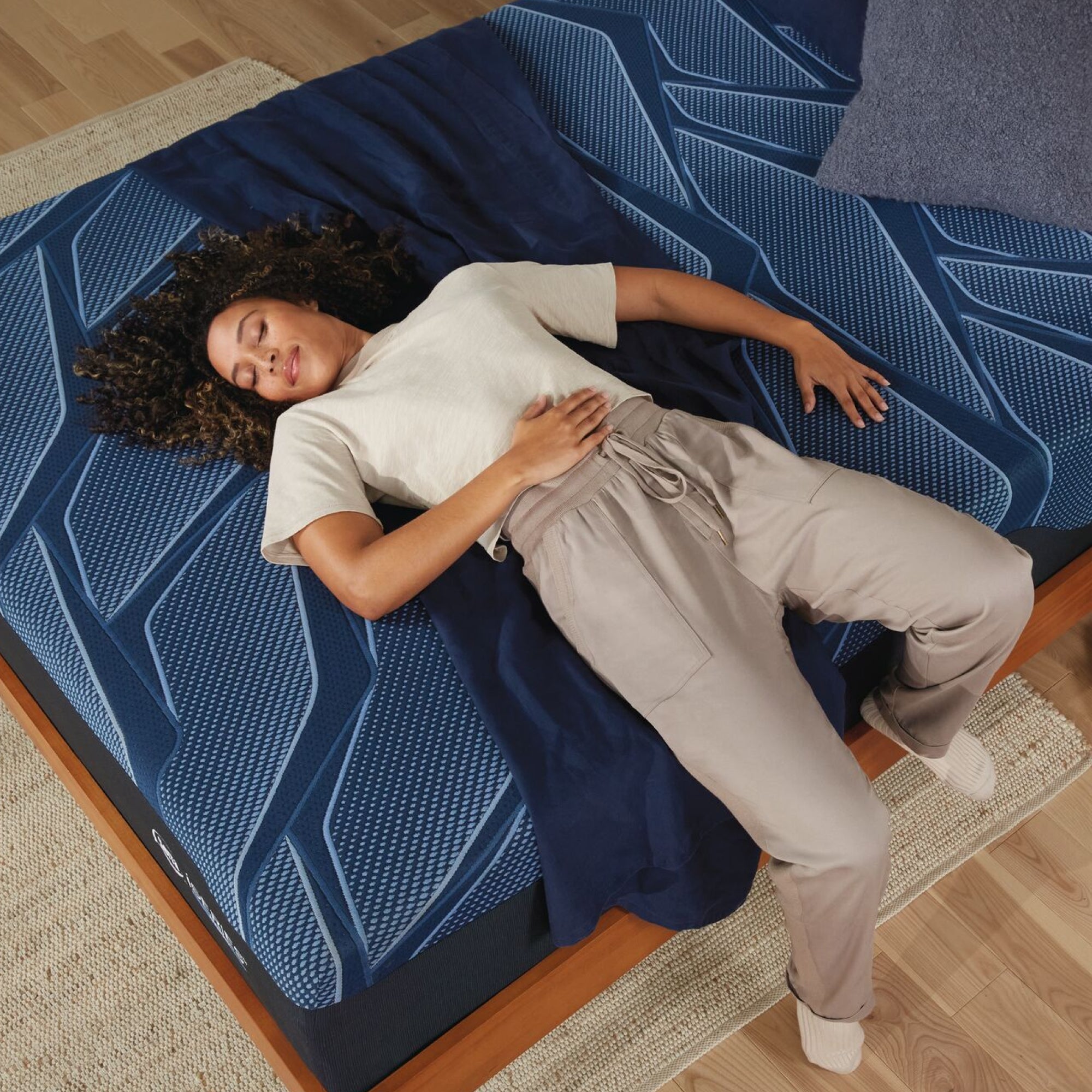 A woman laying on her back on a Serta iSeries medium blue mattress with a blue blanket under it and a blue-grey pillow at the head of the bed||feel: medium||level: Ultimate