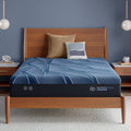 Blue Serta iSeries NXG mattress on a wooden bed frame with pillows against a blue wall.