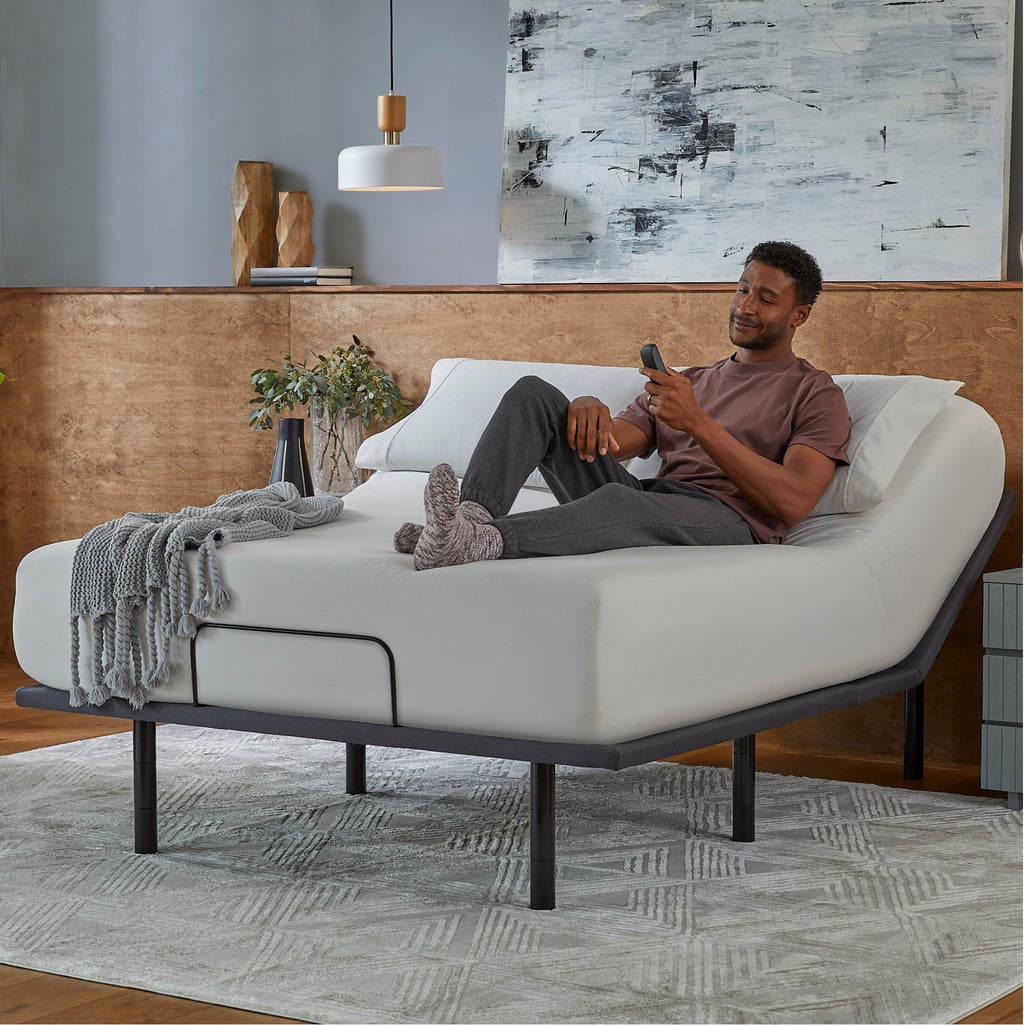 Man sitting in a Baselogic Silver Adjustable Base with a white mattress on top of it.