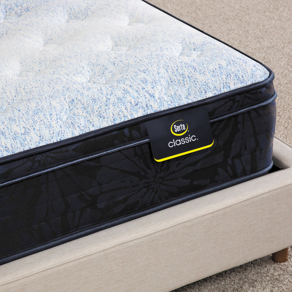 Corner of Serta classic dorian plush euro top mattress sitting in a beige bed frame ||feel: plush euro top ||level: standard